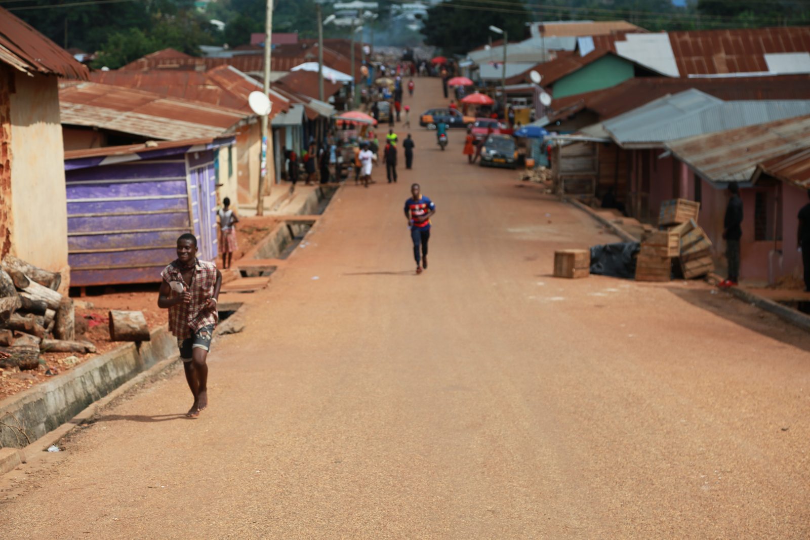 A lone runner coming down a long red dirt road through the village