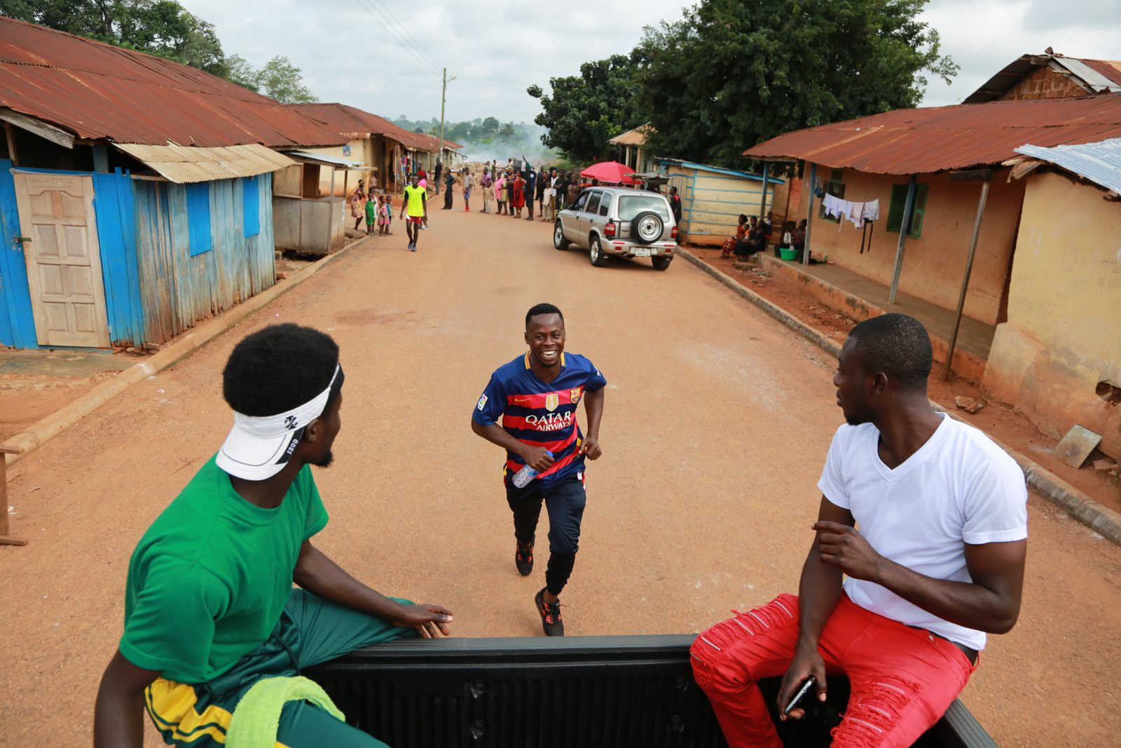 Runners passing through the village while neighbors watch from a truck