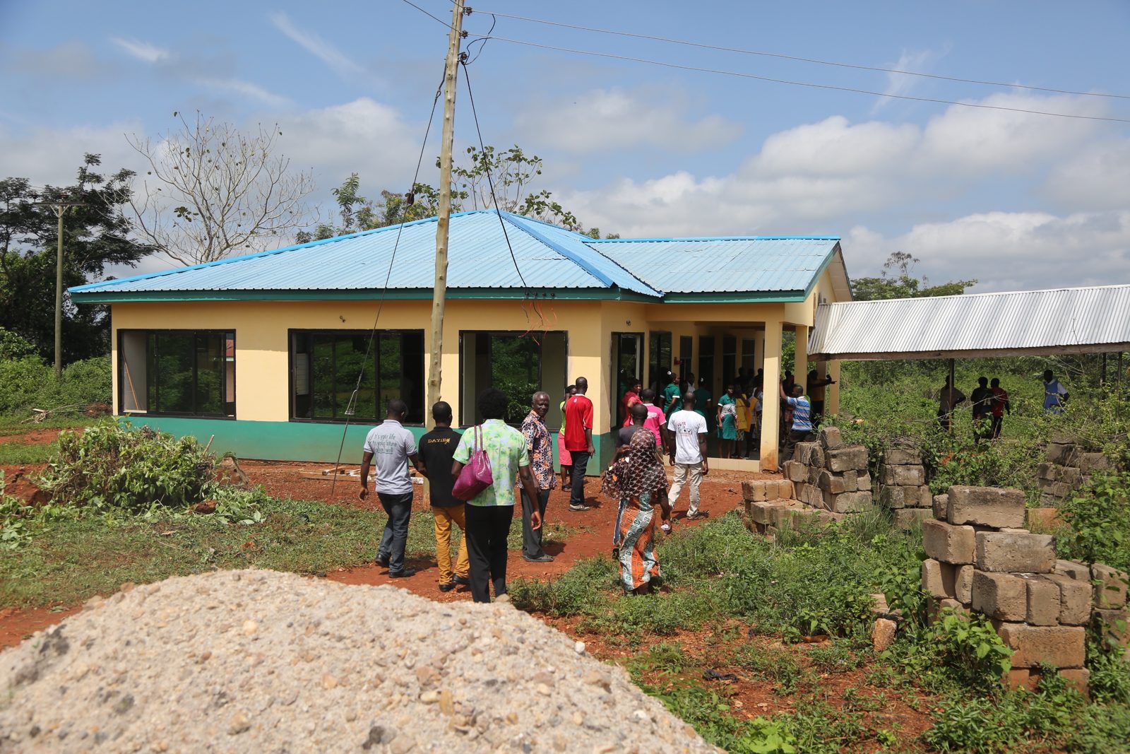 A clinic building with a bright blue roof, community members working outside
