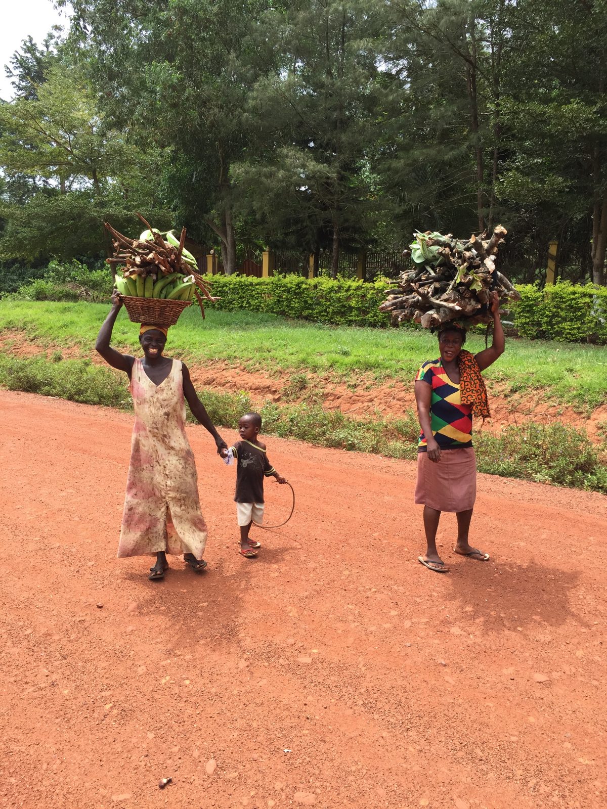 Women carrying goods along a red dirt road