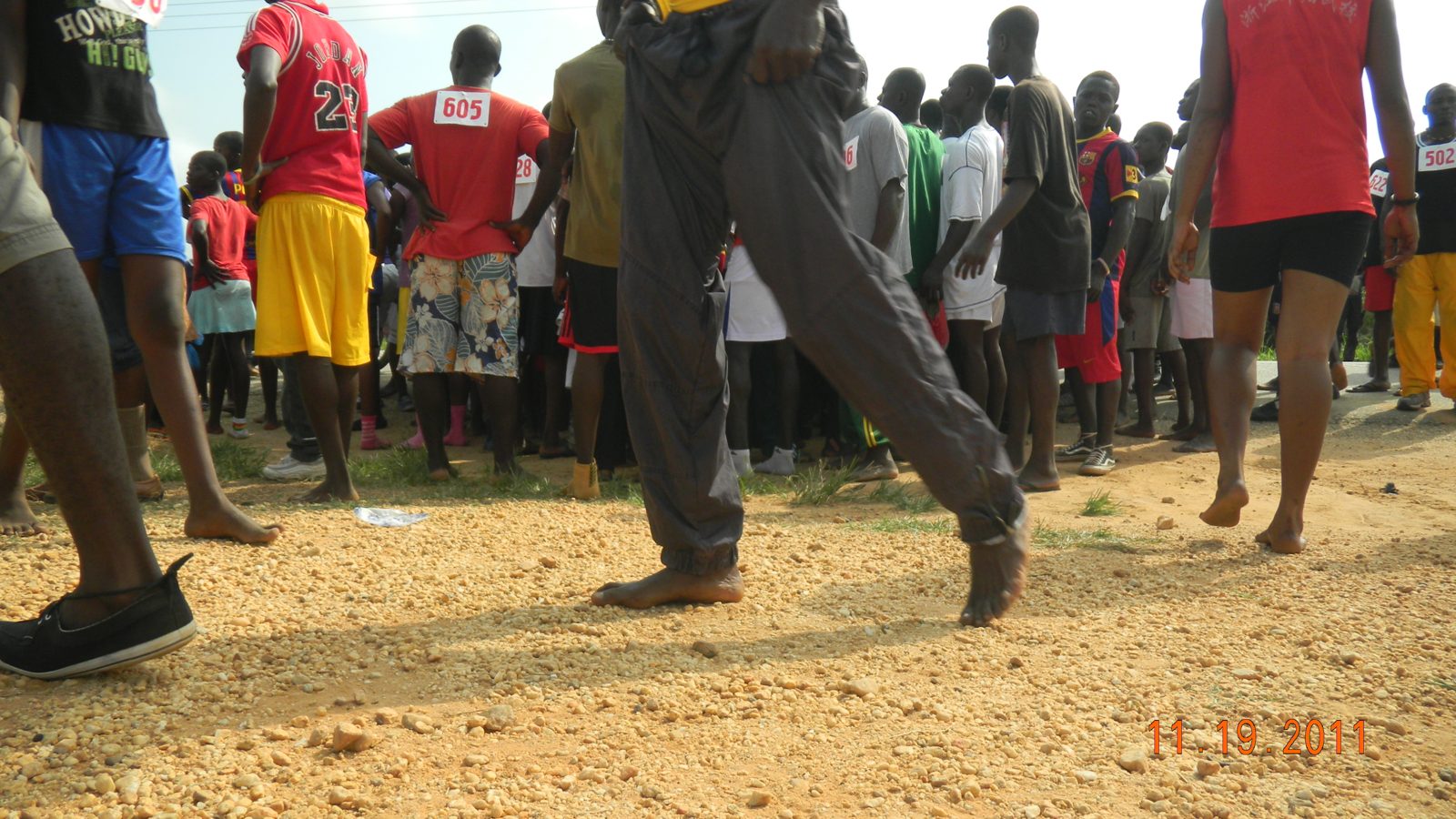 A barefoot runner striding across gravel to the start
